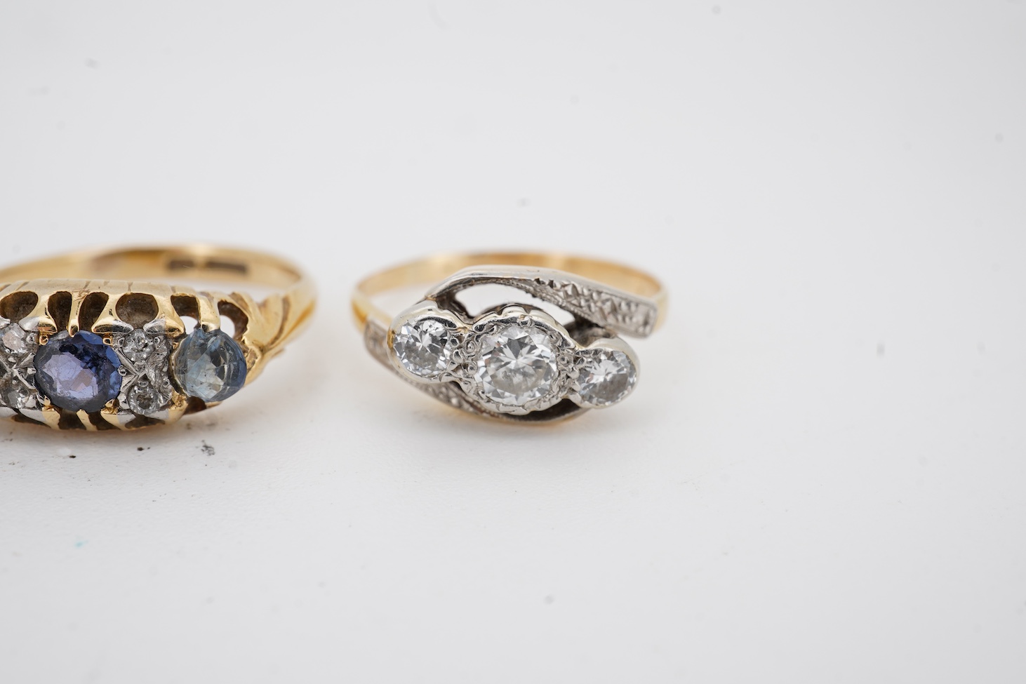 A yellow metal and illusion set three stone diamond crossover ring, size I, an 18ct, sapphire and diamond chip set ring, a modern 18ct gold and six stone sapphire set ring, with diamond chip border and an engraved white